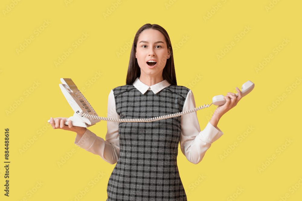 Young surprised secretary with telephone on yellow background Young surprised secretary with telephone on yellow background