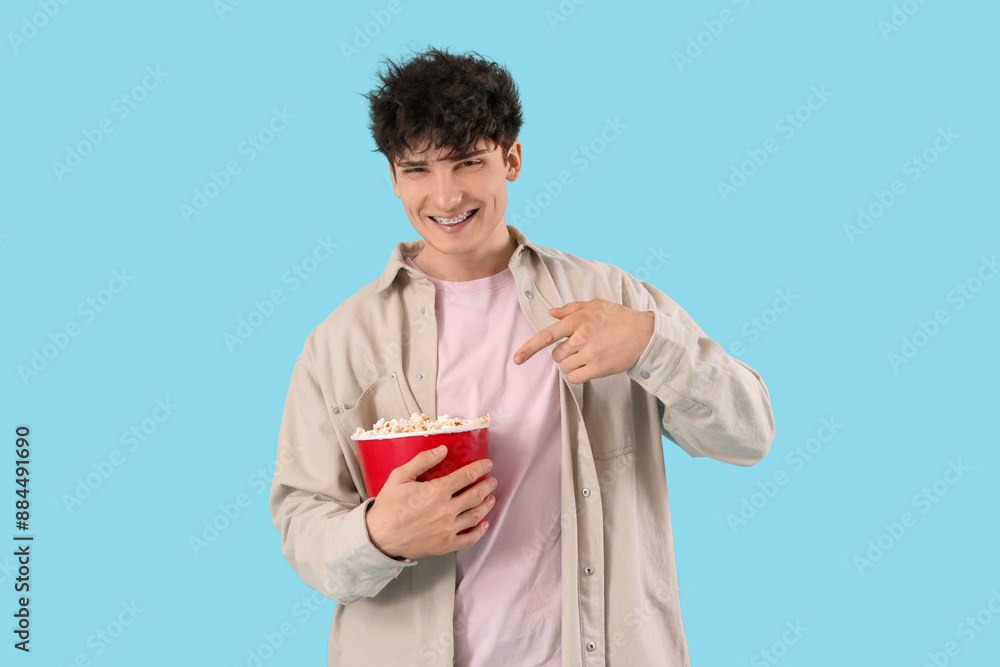 Young man pointing at popcorn on blue background Young man pointing at popcorn on blue background