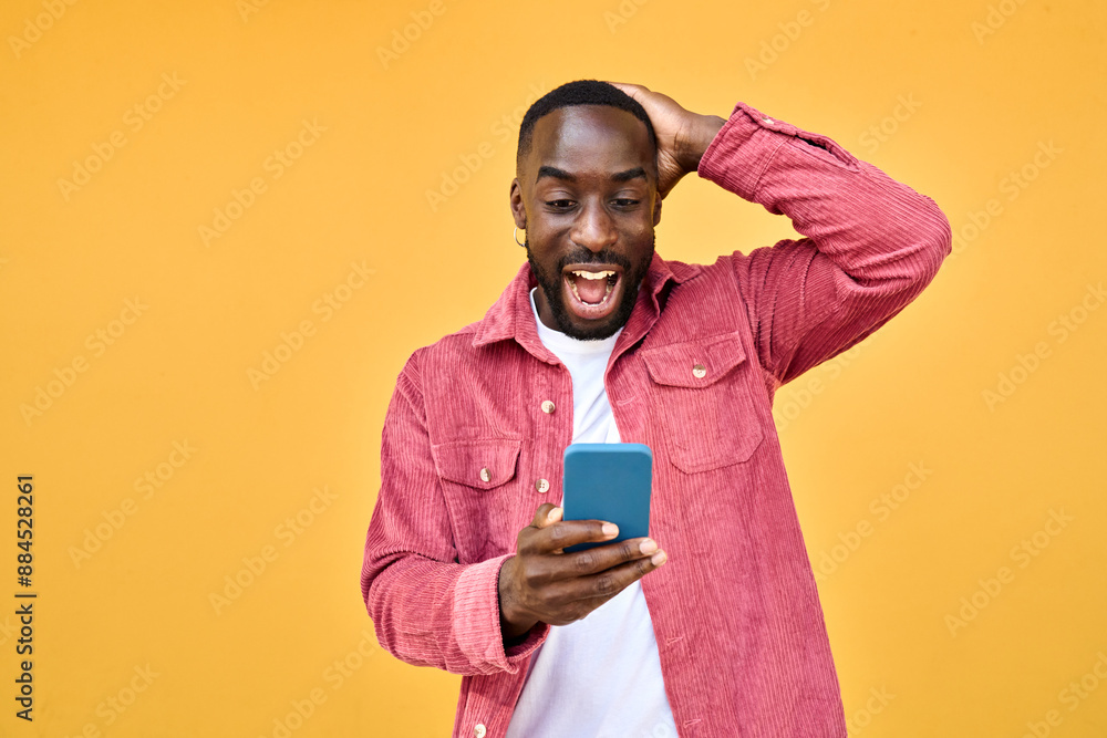 Excited Black man looking at smartphone with wow reaction isolated on yellow. Happy African young gen z guy holding cellphone reading message on cell phone. Amazed user winner using mobile phone Excited Black man looking at smartphone with wow reaction isolated on yellow. Happy African young gen z guy holding cellphone reading message on cell phone. Amazed user winner using mobile phone
