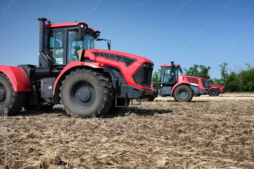 Side view of several large modern red tractors standing in a field. Side view of several large modern red tractors standing in a field.