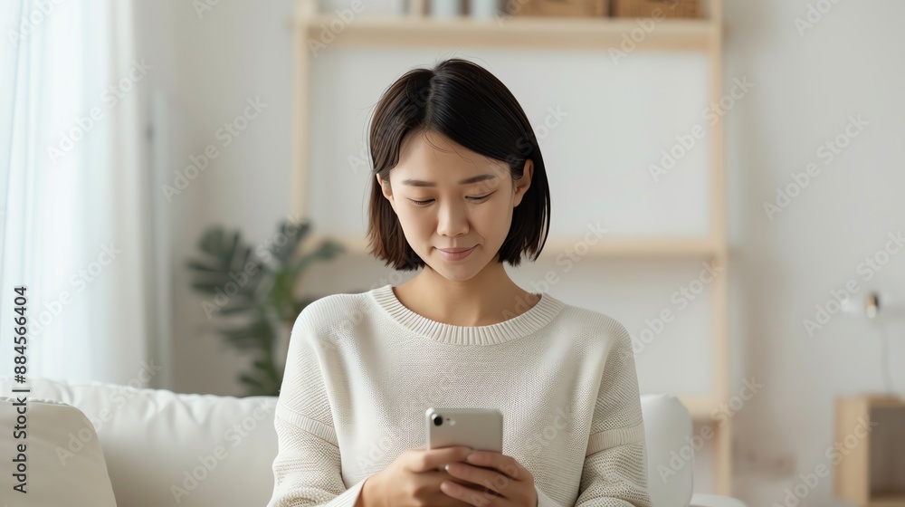 Young woman using smartphone and sitting on sofa in bright living room, smiling and looking at device screen. Young woman using smartphone and sitting on sofa in bright living room, smiling and looking at device screen.