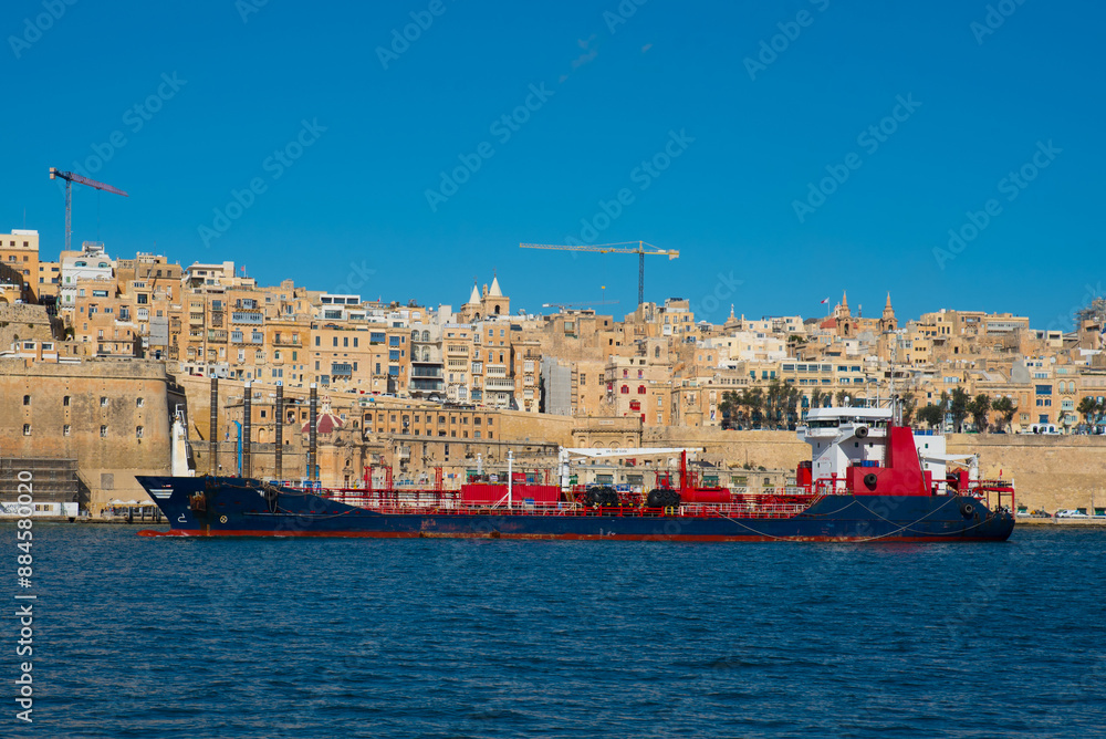 Blue and red cargo ship with beautiful buildings of Valletta in the background Blue and red cargo ship with beautiful buildings of Valletta in the background