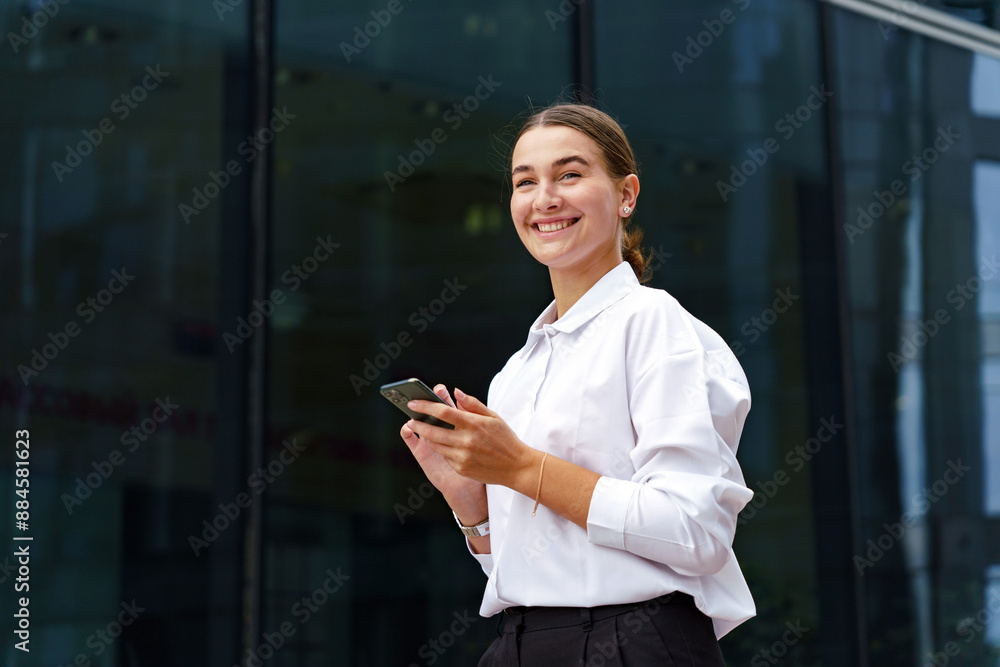 A young professional woman, joyfully holding her phone, stands before a sleek glass building, exuding confidence. A young professional woman, joyfully holding her phone, stands before a sleek glass building, exuding confidence.
