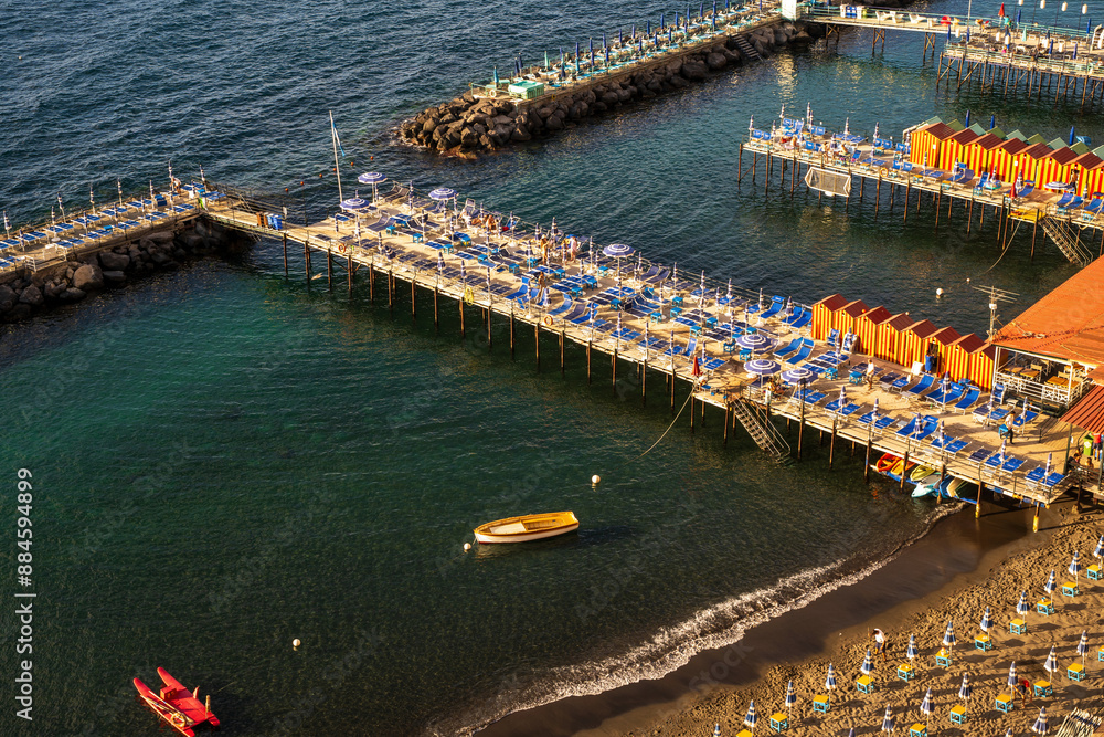 Sorrento, Italy - June 20, 2024: Beautiful coastal view of a marina in Sorrento, Italy with boats, piers, and vibrant striped beach huts against water body