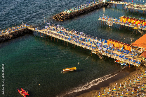 Obraz na płótnie Sorrento, Italy - June 20, 2024: Beautiful coastal view of a marina in Sorrento, Italy with boats, piers, and vibrant striped beach huts against water body w salonie