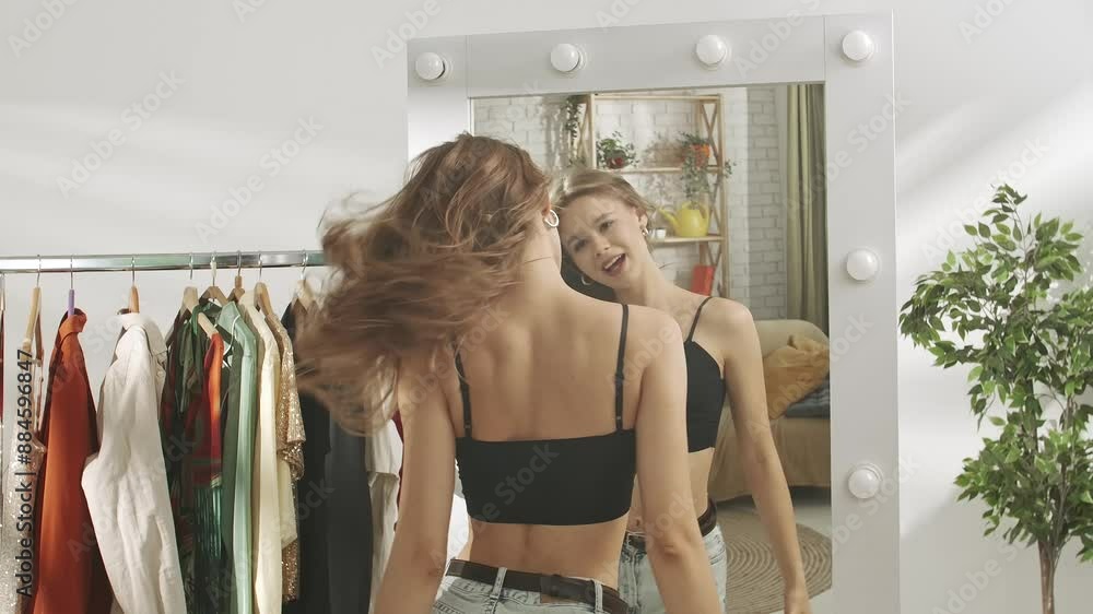 Young millennial woman in her bedroom looks in the mirror, happily dancing and posing, enjoying her look. Self care healthy beauty concept. Young millennial woman in her bedroom looks in the mirror, happily dancing and posing, enjoying her look. Self care healthy beauty concept.