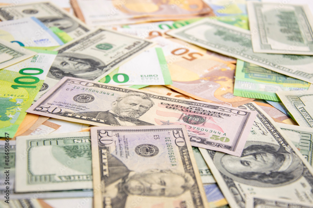A scattering of US dollar bills and Euro banknotes on a white surface A scattering of US dollar bills and Euro banknotes on a white surface