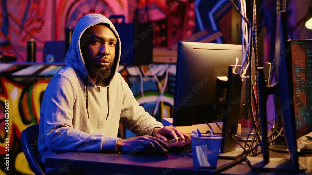 Portrait of african american hacker in abandoned warehouse using phishing technique that tricks users into revealing sensitive information. Hooded cybercriminal stealing passwords Portrait of african american hacker in abandoned warehouse using phishing technique that tricks users into revealing sensitive information. Hooded cybercriminal stealing passwords
