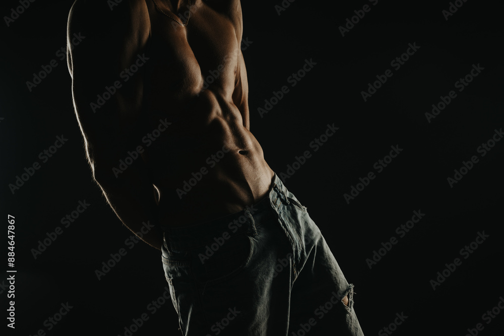 Close-up of a fit, muscular shirtless man in jeans, highlighting his defined abs and physique with dramatic, dark lighting. Close-up of a fit, muscular shirtless man in jeans, highlighting his defined abs and physique with dramatic, dark lighting.