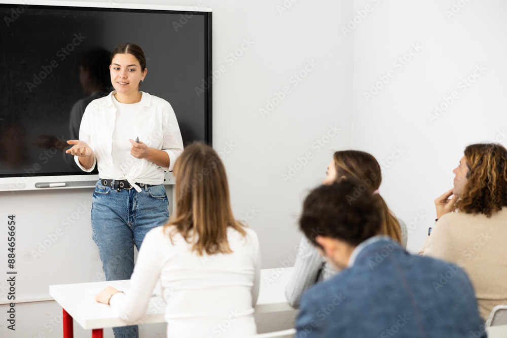 Fototapeta premium Young female tutor teaching students in college classroom