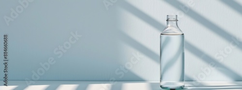 A minimalist scene of a water bottle on a white surface with a sunny window light photo