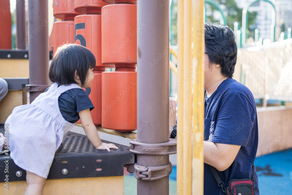 A one-year-old Chinese Malaysian girl playing on the children's playground equipment with her thirty-something father at KLCC Park in Kuala Lumpur City Centre, Malaysia. A one-year-old Chinese Malaysian girl playing on the children's playground equipment with her thirty-something father at KLCC Park in Kuala Lumpur City Centre, Malaysia.