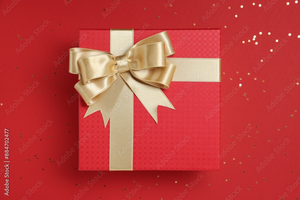 Gift box with bow and confetti on red background, top view Gift box with bow and confetti on red background, top view
