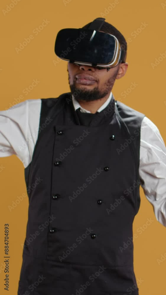 Vertical Video Restaurant waiter uses virtual reality headset with artificial intelligence, having fun with technology and vr glasses against yellow background. Employee with apron and uniform. Camera Vertical Video Restaurant waiter uses virtual reality headset with artificial intelligence, having fun with technology and vr glasses against yellow background. Employee with apron and uniform. Camera