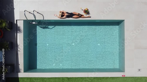 Dark haired slim woman lying at the edge of a beautiful outdoor pool - she wears a dark swimming suit and enjoys the sun photo