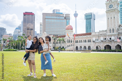 Photography Two thirty-something Indian Malaysian mothers and their seven-year-old son and five-year-old daughter playing joyfully on the expansive lawn at Merdeka Square in Kuala Lumpur, Malaysia