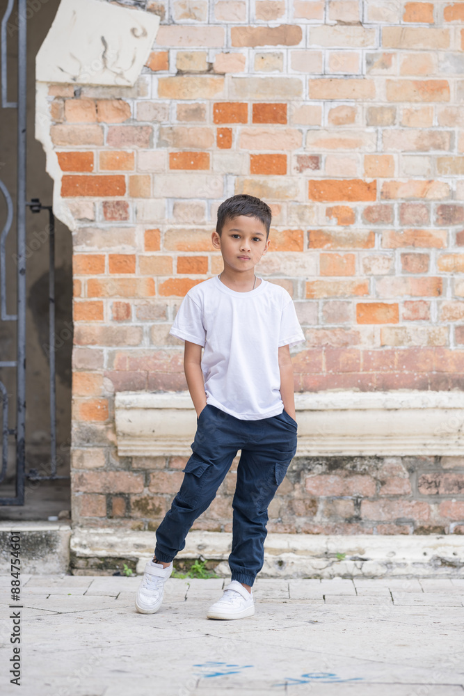 A 7-year-old Indian Malaysian boy wearing a white T-shirt, denim jeans, and white sneakers posing in front of a Western-style brick historical building in Kuala Lumpur, Malaysia, on a hot day. A 7-year-old Indian Malaysian boy wearing a white T-shirt, denim jeans, and white sneakers posing in front of a Western-style brick historical building in Kuala Lumpur, Malaysia, on a hot day.