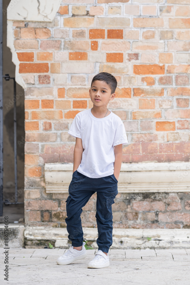 A 7-year-old Indian Malaysian boy wearing a white T-shirt, denim jeans, and white sneakers posing in front of a Western-style brick historical building in Kuala Lumpur, Malaysia, on a hot day. A 7-year-old Indian Malaysian boy wearing a white T-shirt, denim jeans, and white sneakers posing in front of a Western-style brick historical building in Kuala Lumpur, Malaysia, on a hot day.