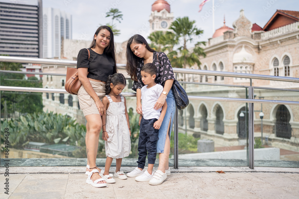 Obraz premium Two 30-something Indian Malaysian mothers with their 7-year-old son and 5-year-old daughter spending time joyfully on a bridge in City Centre, Kuala Lumpur, Malaysia.