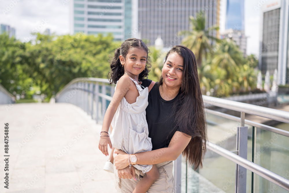 Obraz premium A 30-something Indian Malaysian mother wearing a miniskirt and her 5-year-old daughter in a white dress spending time joyfully on a bridge in City Centre, Kuala Lumpur, Malaysia.