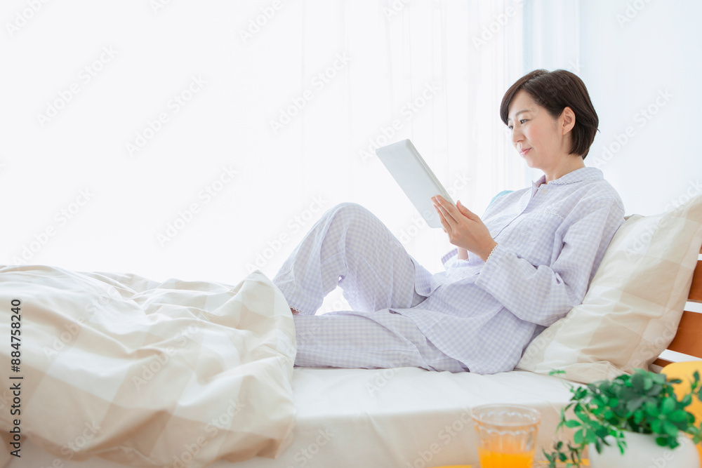 ベッドでタブレットを操作する女性 ベッドでタブレットを操作する女性