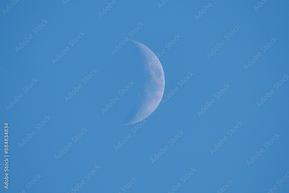 Partial moon on a blue sky with visible craters. Partial moon on a blue sky with visible craters.