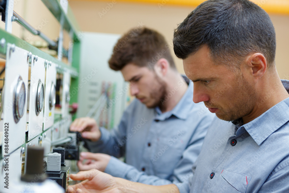 two male technicians working on electrical panel with dials two male technicians working on electrical panel with dials