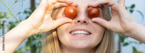 Smiling agriculture worker holding tomatoes over eyes in greenhouse. Fresh seasonal vegetables harvest. Food produce and cultivation. Sustainable farming