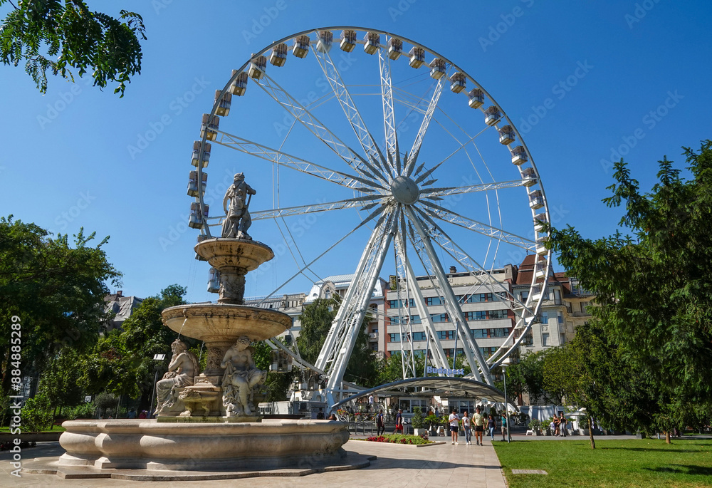 Obraz premium Budapest, Hungary - September 2, 2023: Low angle and summer view of Danubius Fountain and tourists on the square against a ferris wheel 