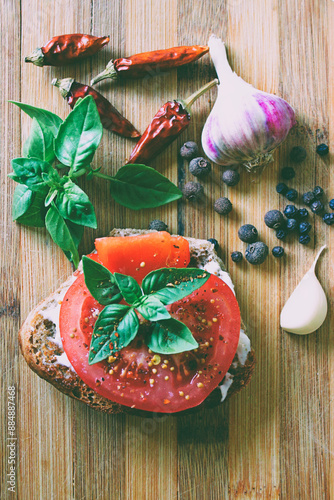 Sandwich with tomato, fresh basil and spices on wooden desk with garlic, scattered peppercorns and dried hot pepper old style photo
 photo