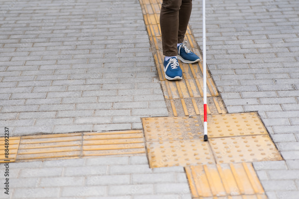 Close-up of a woman's legs with a cane near a tactile tile. Close-up of a woman's legs with a cane near a tactile tile.