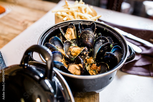 Bowl of cooked mussels with a side of fries on a wooden table. photo