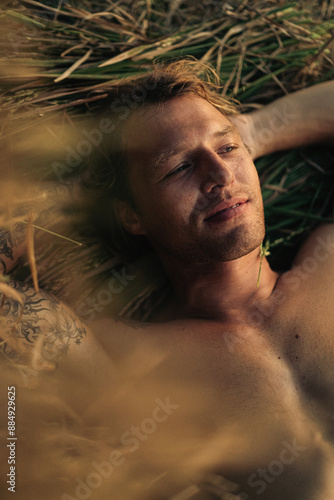 Young romantic dreaming man lies in a field in the hay at sunset.