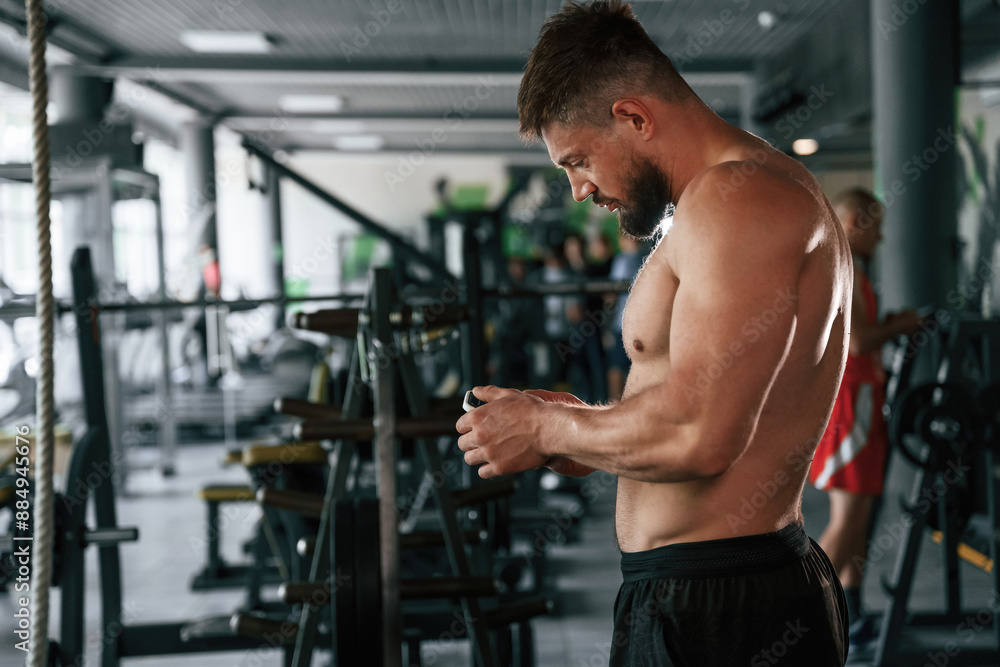 With smartphone, taking a break. Strong muscular man is working out in the gym With smartphone, taking a break. Strong muscular man is working out in the gym