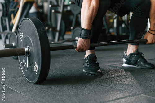 Big and heavy barbell in hands. Strong muscular man is working out in the gym