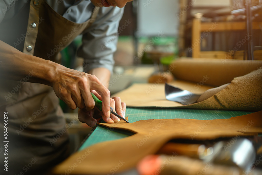 Cropped shot of artisan working on the workbench with different rolls brown leather Cropped shot of artisan working on the workbench with different rolls brown leather