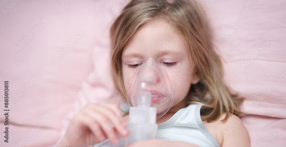 Portrait of sad little girl having inhalation for easing cough. Child in medical oxygen mask lying in bed. Labored breathing, lack of oxygen or inhalation concept Portrait of sad little girl having inhalation for easing cough. Child in medical oxygen mask lying in bed. Labored breathing, lack of oxygen or inhalation concept