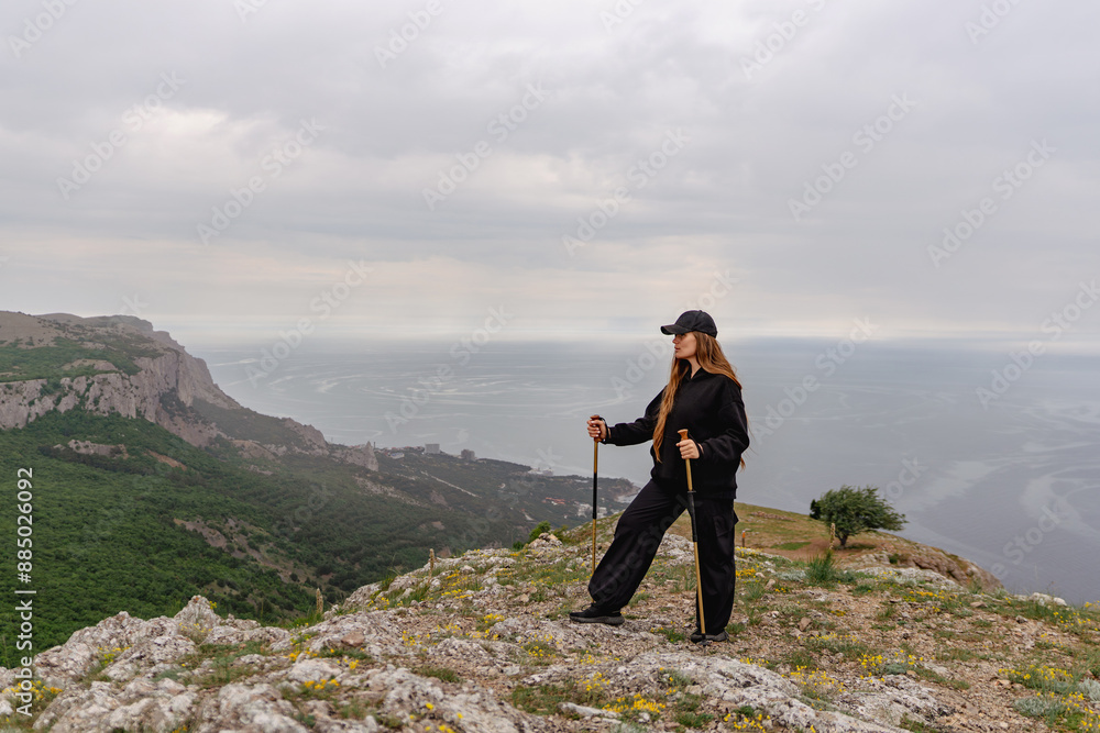 Obraz premium A woman stands on a mountain top with her arms crossed and a hat on