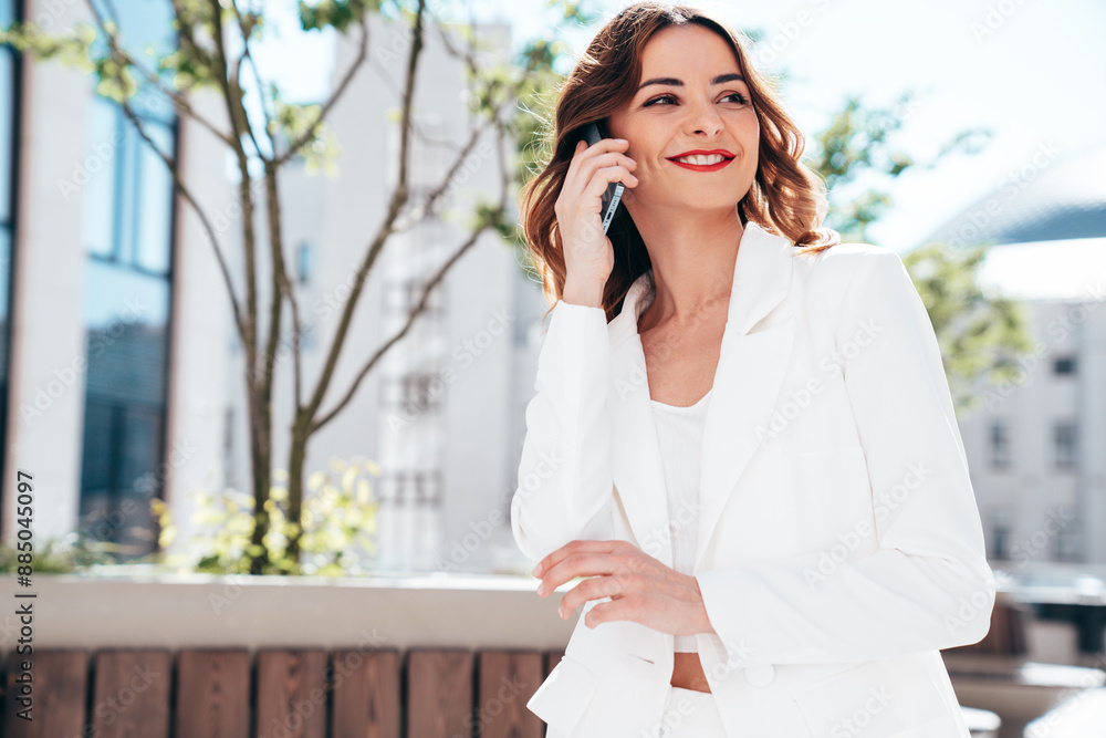 Young beautiful brunette woman wearing nice trendy white suit jacket. Sexy smiling model posing in the street. Fashionable female using mobile phone. Makes call, chatting. Talks, speaks at smartphone Young beautiful brunette woman wearing nice trendy white suit jacket. Sexy smiling model posing in the street. Fashionable female using mobile phone. Makes call, chatting. Talks, speaks at smartphone
