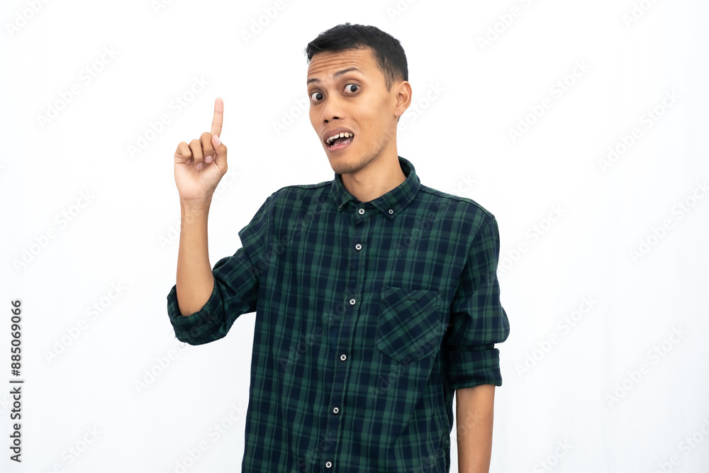 Asian man wearing a green checkered casual shirt pointing towards an empty space for advertising. Isolated white background. Asian man wearing a green checkered casual shirt pointing towards an empty space for advertising. Isolated white background.