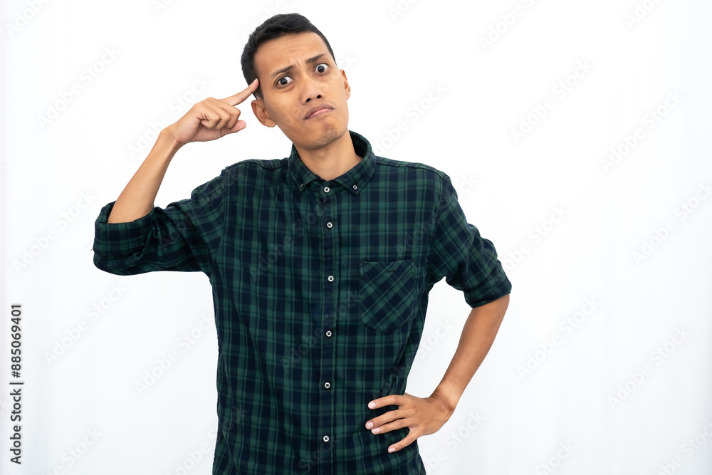 An Asian man wearing a casual green checkered shirt gave off an angry expression while pointing his finger at his brain to tell it to think. Isolated white background. An Asian man wearing a casual green checkered shirt gave off an angry expression while pointing his finger at his brain to tell it to think. Isolated white background.