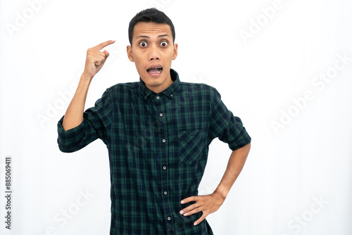 An Asian man wearing a casual green checkered shirt gave off an angry expression while pointing his finger at his brain to tell it to think. Isolated white background.