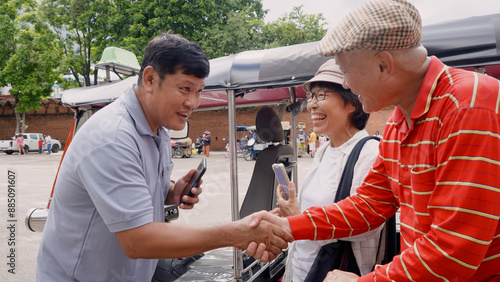 Local tuk-tuk driver shaking hands with elderly tourists in Chiang Mai, Thailand. Man in blue shirt, woman in hat and glasses. Scene of friendly interaction and local transportation service.