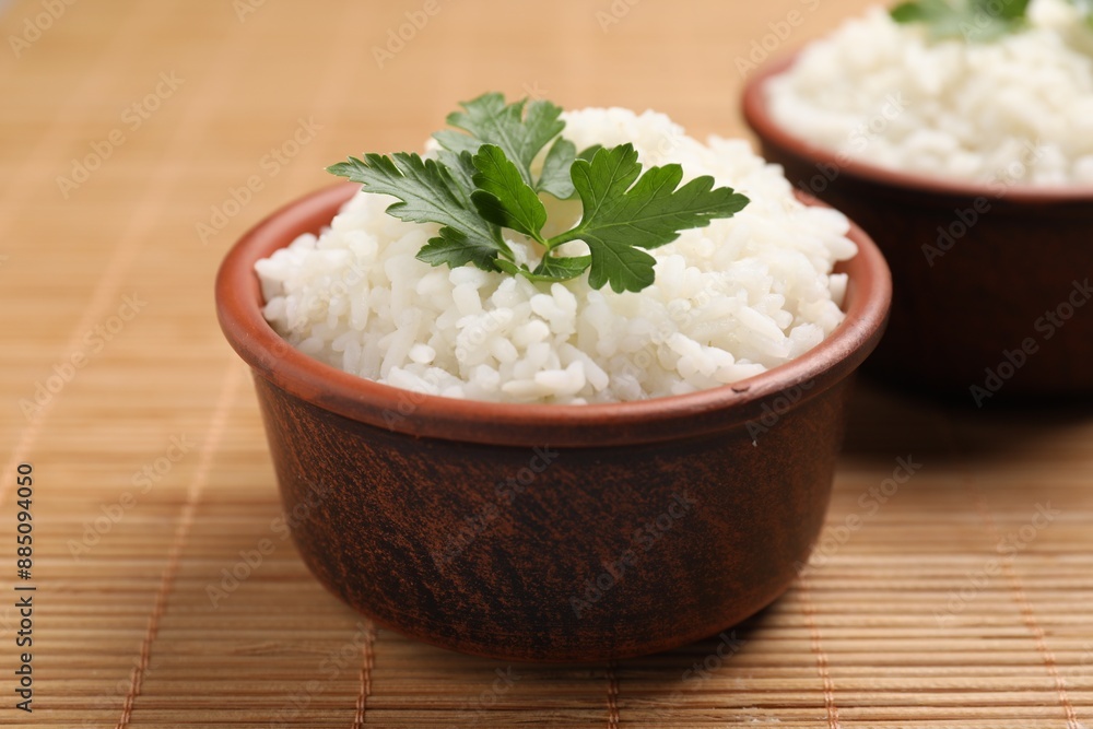 Bowls of delicious boiled rice with parsley on bamboo mat, closeup Bowls of delicious boiled rice with parsley on bamboo mat, closeup
