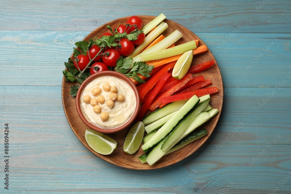 Tasty homemade hummus and different vegetables served on light blue wooden table, top view Tasty homemade hummus and different vegetables served on light blue wooden table, top view