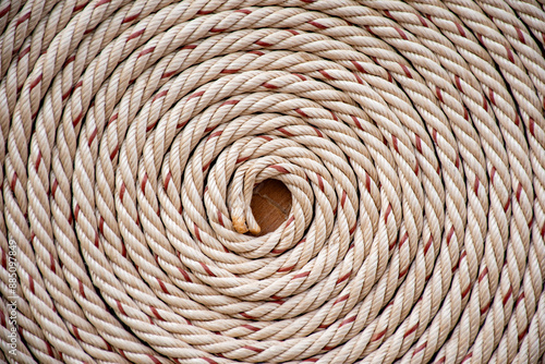 White rope with red lines and coiled roll from top view on wooden table background in warm tone. Braided rope on a roll background texture 2025. Photo of an old vintage rope.