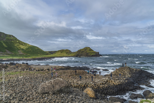 Giant's Causeway, Northern Ireland - August 3, 2023: High angle and summer view of seaside volcanic rocks with tourists standing on columnar joints against wave on the sea
 photo