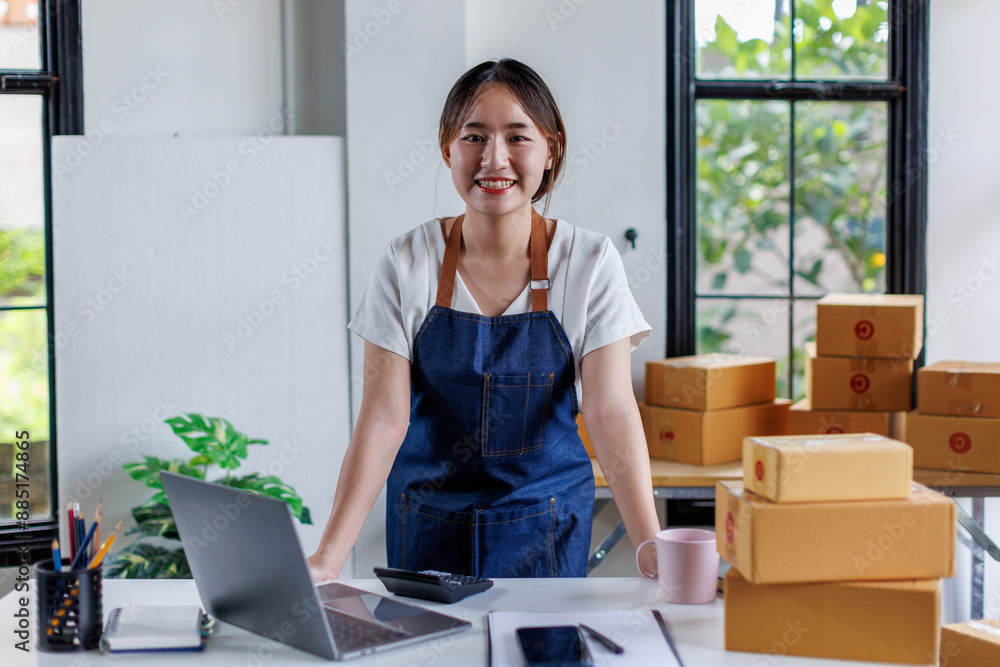 Happy young asian woman startup small business freelance holding parcel box and computer laptop and sitting on chair, Online marketing packing SME box delivery concept Happy young asian woman startup small business freelance holding parcel box and computer laptop and sitting on chair, Online marketing packing SME box delivery concept
