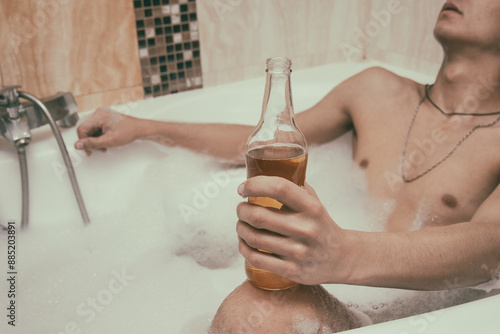 A young attractive man is relaxing in the bathroom and drinking beer.