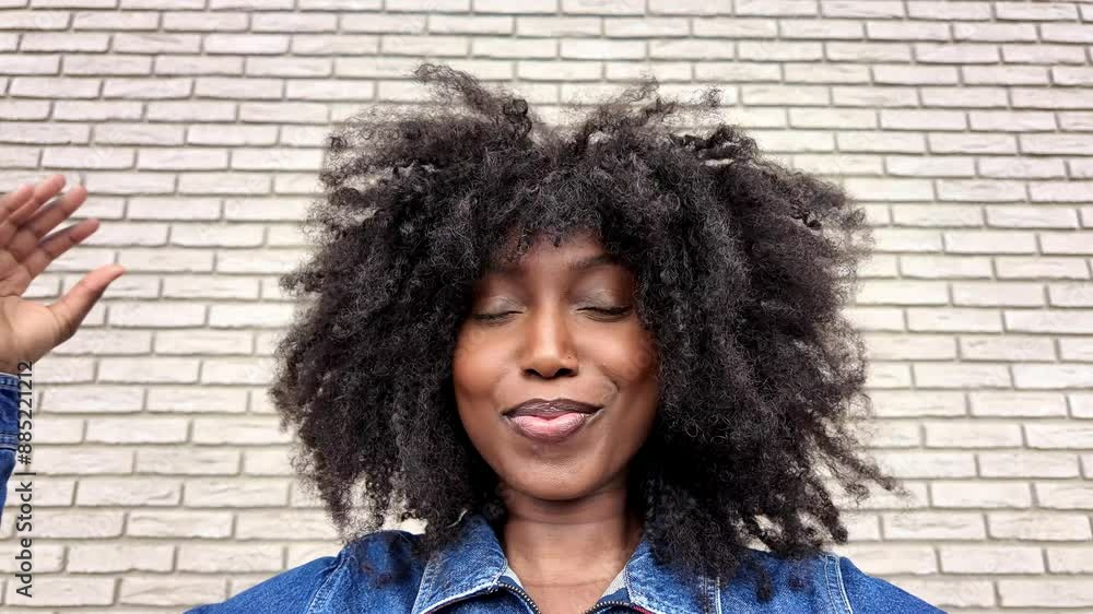 A woman with natural curly hair exudes confidence, wearing a denim jacket, posing stylishly in front of a brick wall A woman with natural curly hair exudes confidence, wearing a denim jacket, posing stylishly in front of a brick wall